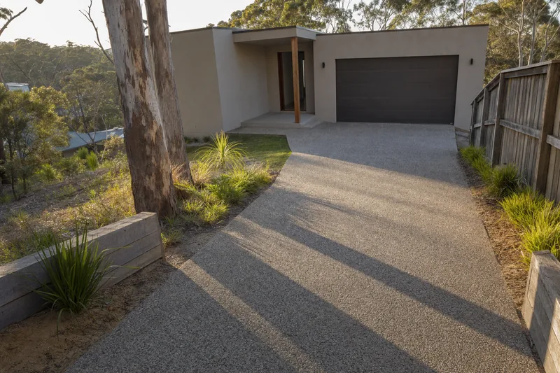 Exposed aggregate driveway showing stone texture at a rendered home on a sloping bushland block — exposed aggregate, Central Coast. Illustrative example.