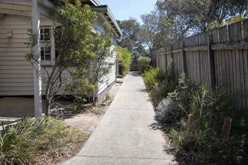 Concrete path running down the side of a weatherboard cottage past coastal wattle and banksia planting — concrete paths & footpaths, Central Coast. Illustrative example.