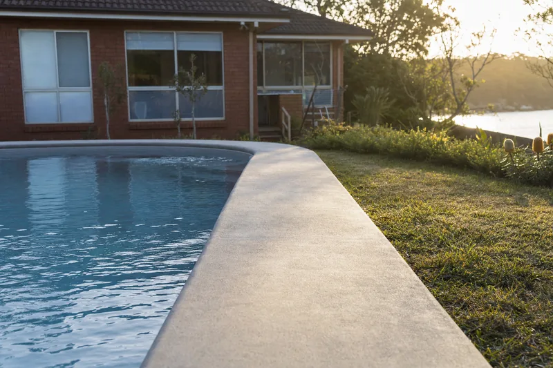Plain concrete pool surround beside a domestic in-ground pool on a flat lake-adjacent block — something else?, Central Coast. Illustrative example.
