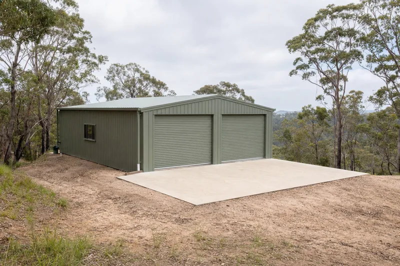 Concrete slab for a Colorbond shed on a sloping bushland block with a ridgeline behind — shed & garage slabs, Central Coast. Illustrative example.