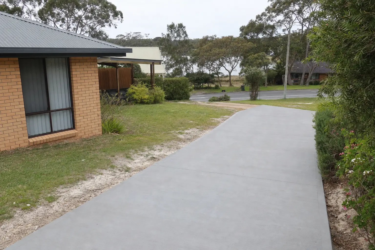 Plain grey concrete driveway at a brick-veneer home on a flat Central Coast block — concreting, Central Coast. Illustrative example.