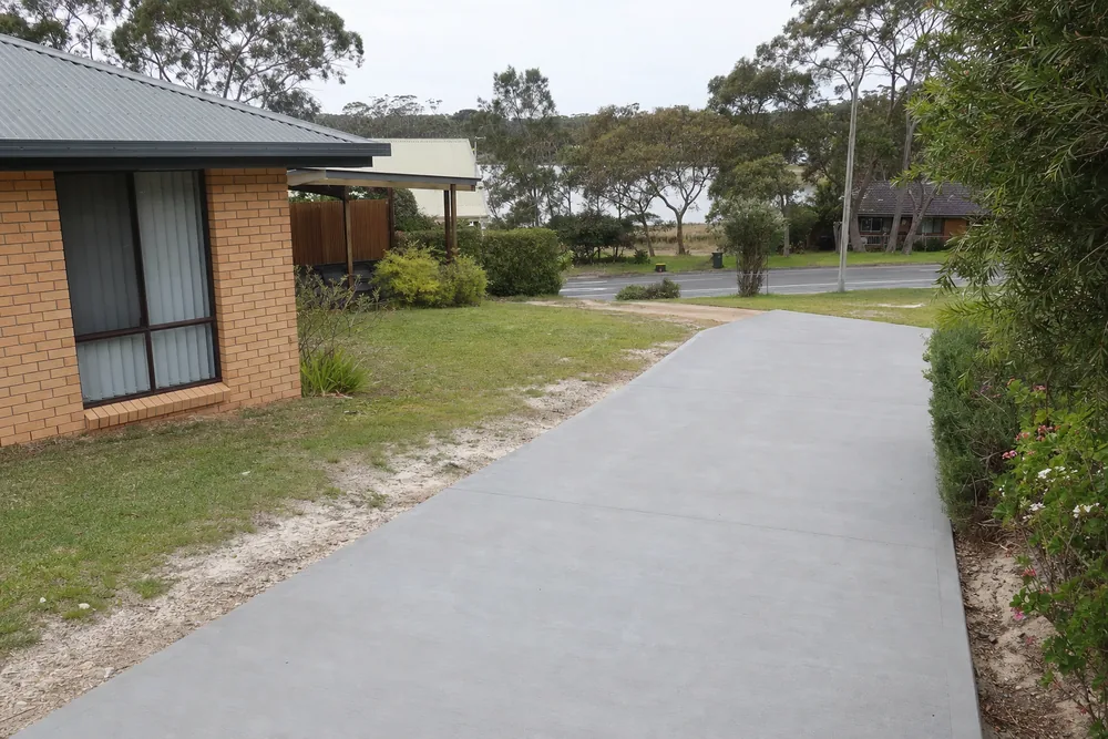 Plain grey concrete driveway at a brick-veneer home on a flat Central Coast block — concreting, Central Coast. Illustrative example.